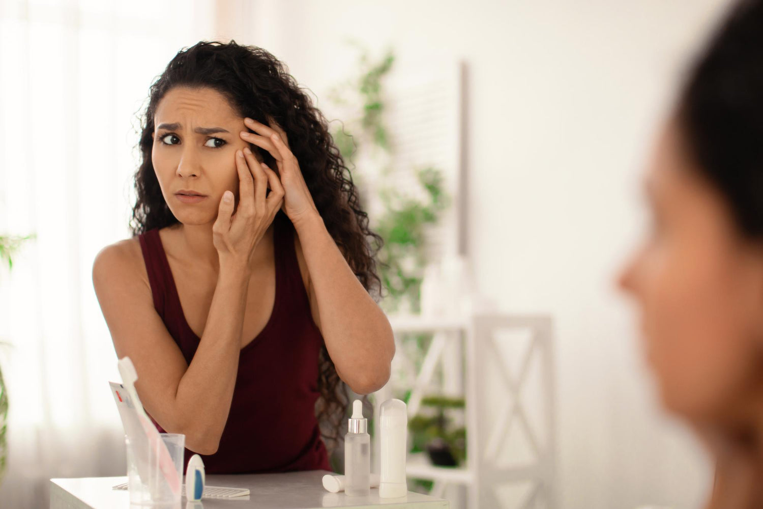 Woman examining skin near eye in mirror with concerned expression